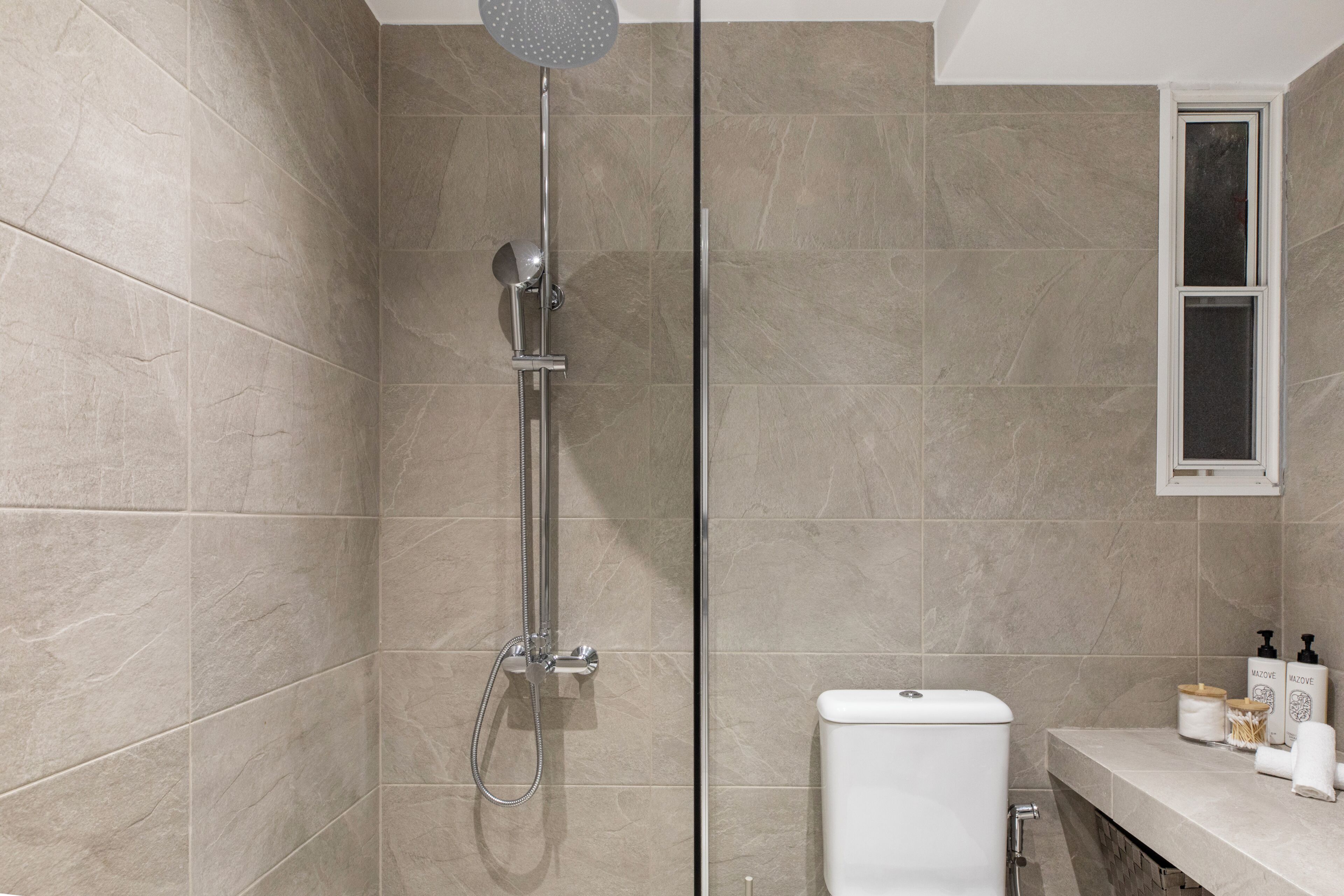 A modern bathroom with a shower, toilet, and a window.