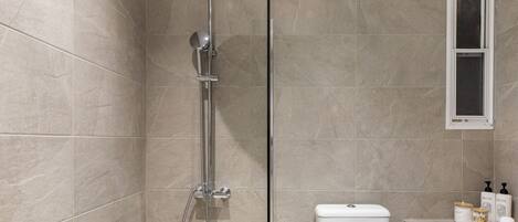 A modern bathroom with a shower, toilet, and a window.