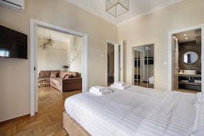 A hotel room with a large bed, a sofa, a TV, and a bathroom with a mirror and sink. - Acropolis Museum View Residence by A&A Residences (Athens)