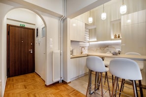 A modern kitchen with white cabinets, a wooden door, a radiator, and two bar stools. - Acropolis Museum View Residence by A&A Residences (Athens)