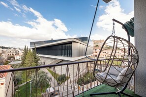 A balcony with a hanging chair, a modern building in the background, and a view of the surrounding area. - Acropolis Museum View Residence by A&A Residences (Athens)