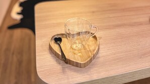 Uma mesa de madeira com uma caneca de vidro e uma colher sobre um apoio para copos em formato de coração.