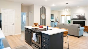 A modern kitchen with a central island, a dining area with a sofa, and a living room with a fireplace. - Hot Tub! Hidden Kayak Cove -2 Masters, Kayaks, Fire pit, & Game Room (Jasper)