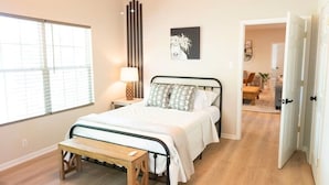 A bedroom with a bed, bedside table, lamp, and a view of the adjacent room. - Hot Tub! Hidden Kayak Cove -2 Masters, Kayaks, Fire pit, & Game Room (Jasper)