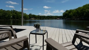 A wooden deck with outdoor seating, a small table with a plant and glass, and a view of a lake. - Hot Tub! Hidden Kayak Cove -2 Masters, Kayaks, Fire pit, & Game Room (Jasper)