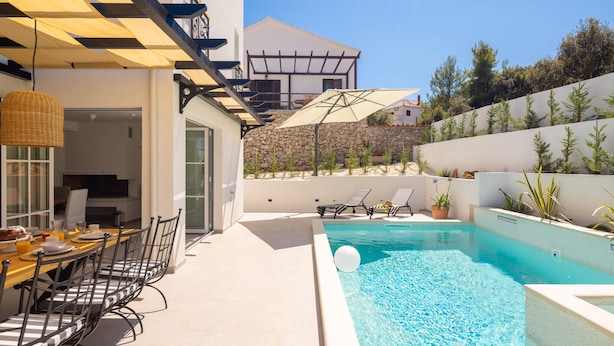 A poolside area with a dining table and chairs, a stone wall, and a view of a building in the background. - Villa Verde Razanj With Heated Pool (Rogoznica)