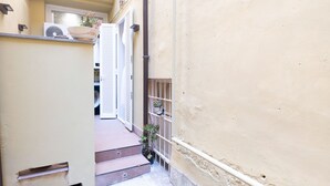 A narrow alleyway with steps leading to a door, a white air conditioning unit, and a potted plant on the right. - Ernesta 3BR Lovely Home by The Spanish Steps (Roma)