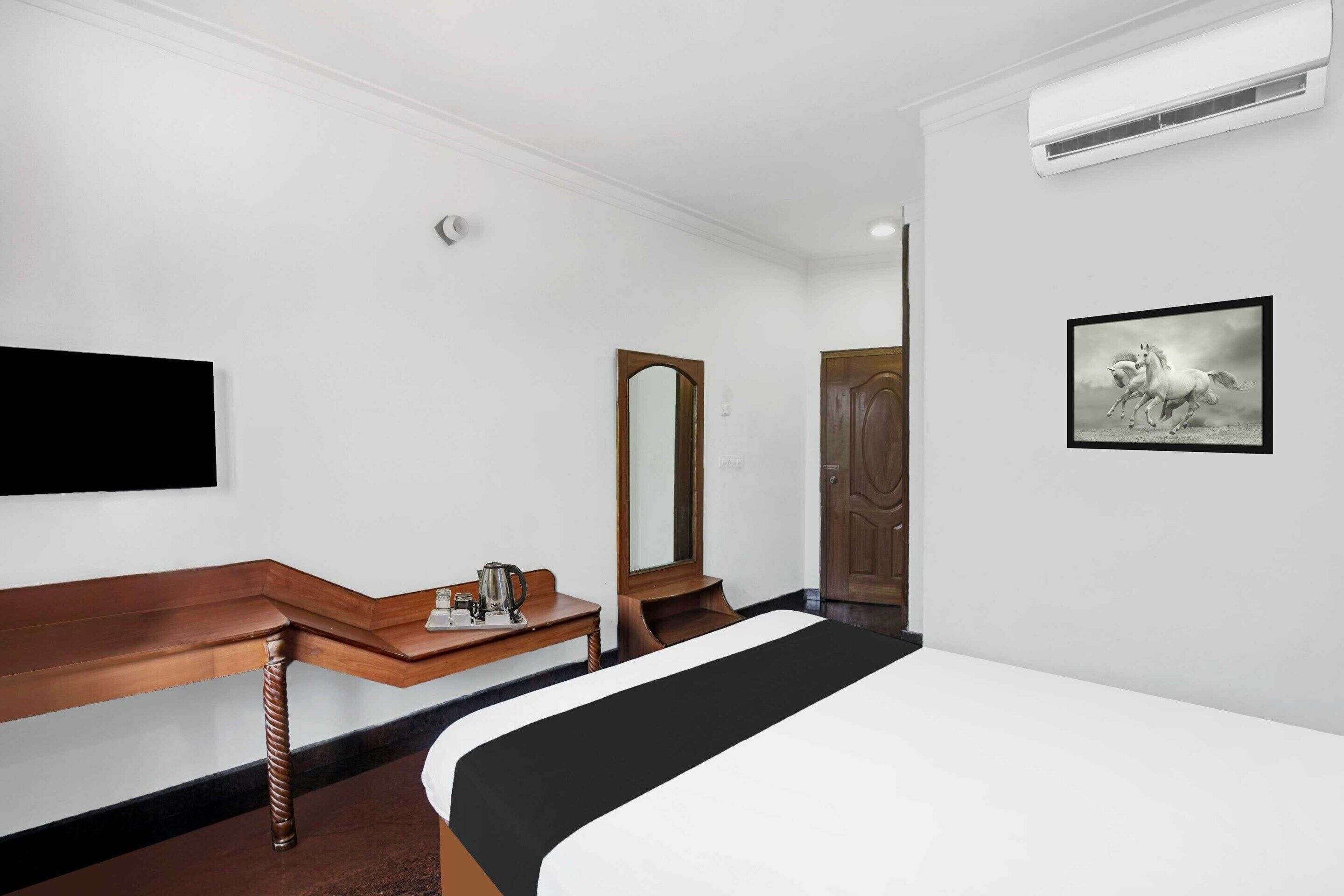 Een hotelkamer met een bed, een houten bankje, een spiegel, een schilderij aan de muur en een airconditioner.