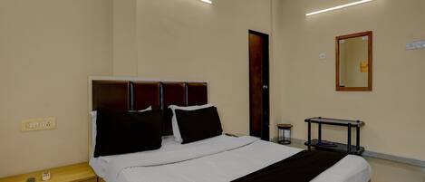A hotel room with a bed, bedside table, nightstand, and a small table with a chair.