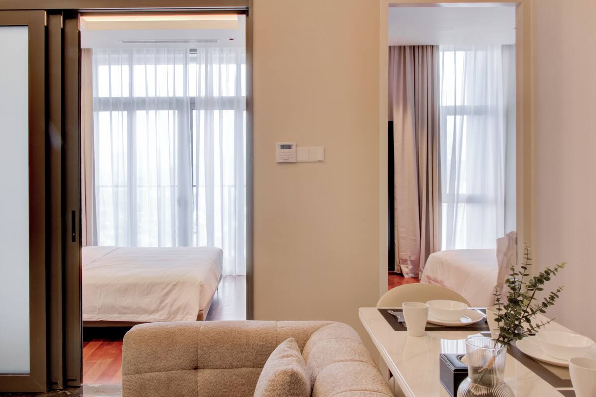 Een hotelkamer met een bed, een slaapbank, een eettafel met een vaas, en een raam met gordijnen.