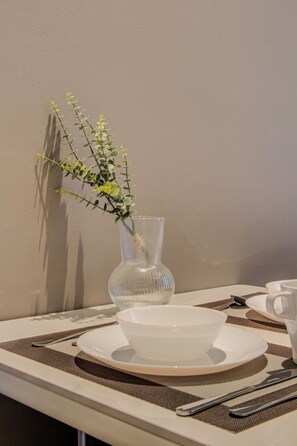 A dining table with a clear glass vase containing green foliage, a white bowl, and a set of cutlery. - Royce Residences KLCC by CREMES KL (Kuala Lumpur)