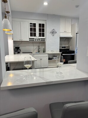 Een moderne keuken met witte kasten, een marmeren aanrechtblad en twee wijnglazen.