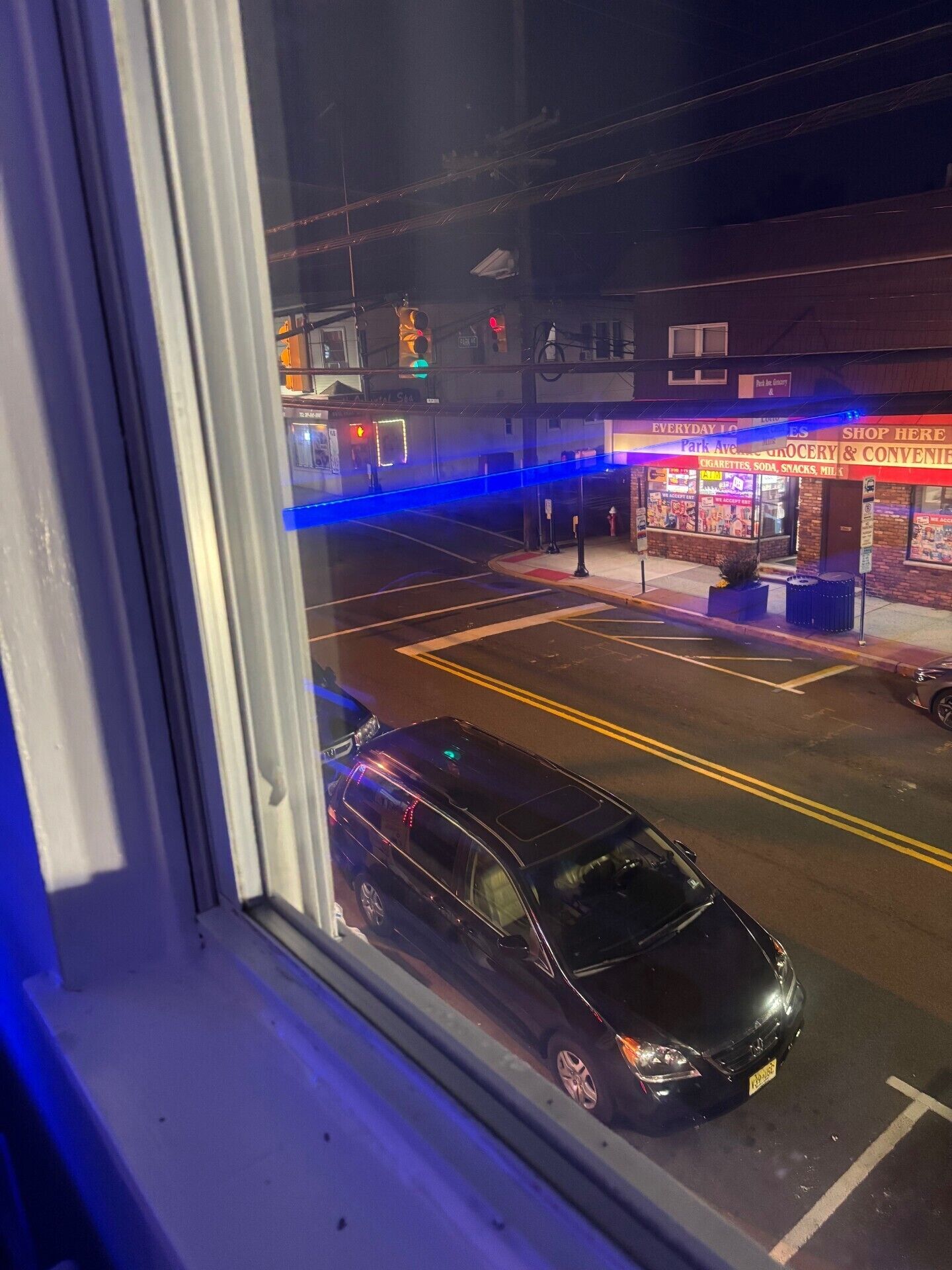 A nighttime street view with a parked car, a traffic light, and a storefront with illuminated signage.