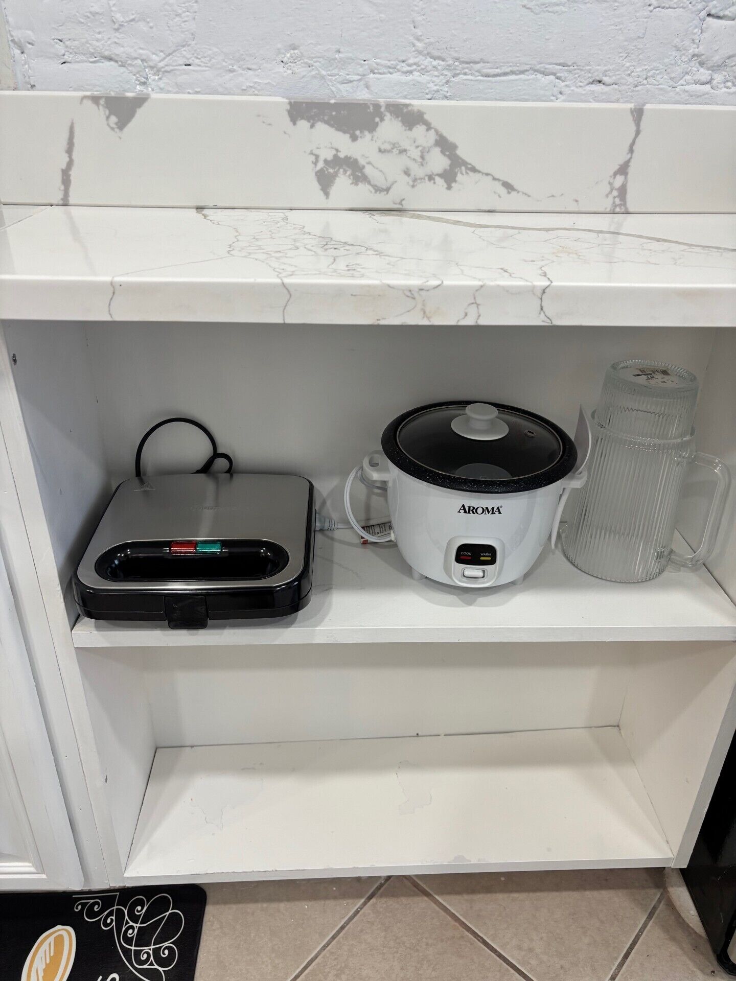 A kitchen shelf with a rice cooker, a coffee maker, and a kettle.