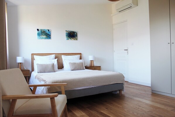Un dormitorio con cama, mesitas de noche, una silla y obras de arte en la pared.