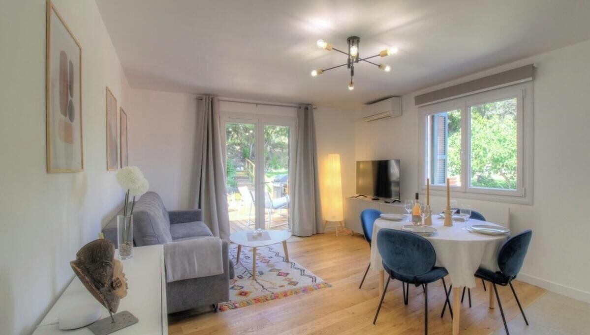 Una sala de estar moderna con un sofá, una mesa de comedor con sillas, un televisor y un ventanal grande.