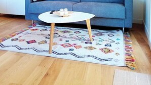 A living room with a blue sofa, a white coffee table, and a patterned rug. - Appartement avec jardin et terrasse (Alata)
