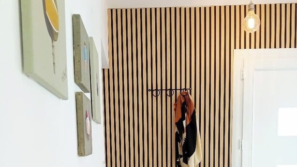 A hallway with a striped wall, a coat rack with a scarf, and a door. - Appartement avec jardin et terrasse (Alata)