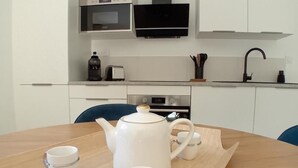 A modern kitchen with white cabinets, a microwave, a black range hood, and a wooden dining table with a tea set. - Appartement avec jardin et terrasse (Alata)