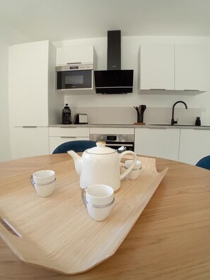 Eine moderne Küche mit weißen Schränken, einer Mikrowelle, einer schwarzen Dunstabzugshaube und einem Holztisch mit Tee-Service.