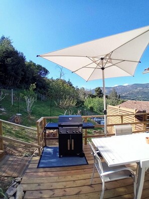 Una terraza de madera con una parrilla, una mesa y una sombrilla que da sombra.