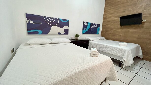 A hotel room with two beds, white bedding, a small potted plant, and abstract wall art.