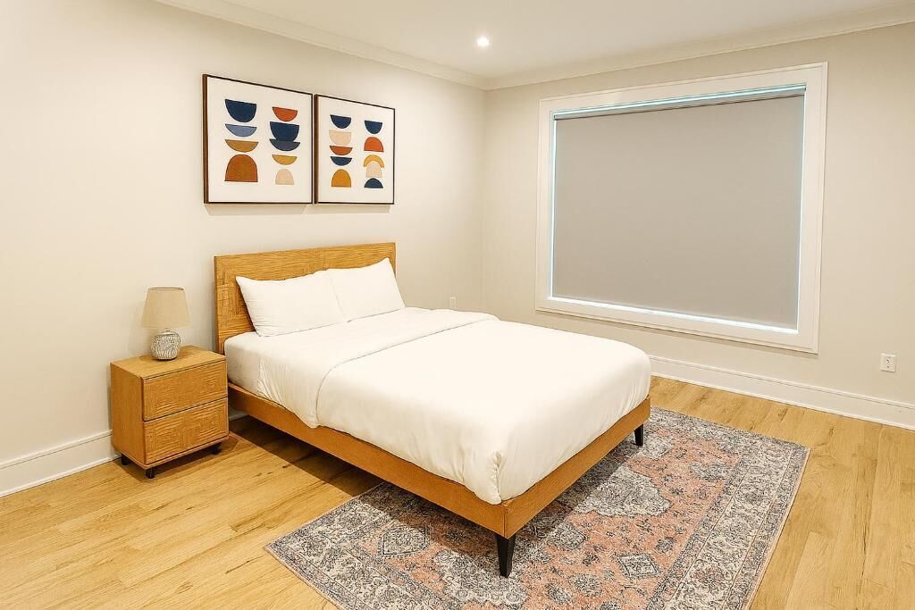 A bedroom with a wooden bed, a nightstand, a patterned rug, and two abstract wall art pieces.