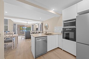 A modern kitchen with a dishwasher, oven, and microwave. There is a dining area with a table and chairs. - Family Friendly 2 Bed Flat With Balcony (Sunshine Coast)
