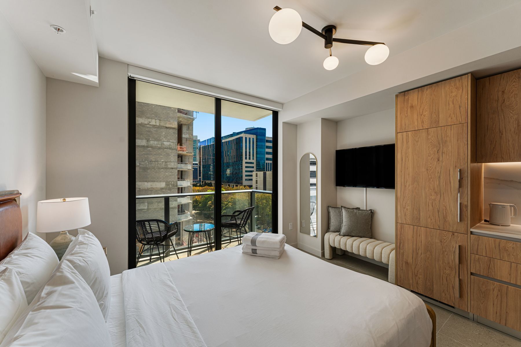 Una camera d'albergo moderna con un letto grande, un balcone con sedie, una TV e un armadio in legno.