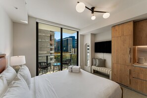 A modern hotel room with a large bed, a balcony with chairs, a TV, and a wooden wardrobe. - Crosby Miami WTC Studio City Nest #602 (Miami)