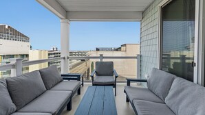 Ein Balkon mit grauen Sofas und einem Holztisch mit Blick auf eine Stadtlandschaft.