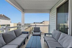 A balcony with grey sofas and a wooden table, overlooking a cityscape. - BEACH BLOCK! ELEVATOR! POOL! SO CLOSE TO BOARDWALK RIDES RESTAURANTS! NEW CONDO! (Wildwood)