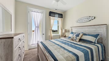 A bedroom with a bed, a dresser, a ceiling fan, a window with curtains, and a welcome sign.