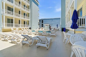 A poolside area with lounge chairs and tables, a small pool, and a building with balconies.
