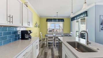 A kitchen with a coffee maker, a sink, and a dining area with chairs.
