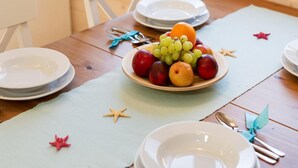 Une table à manger dressée avec des assiettes, un centre de table composé de fruits et des décorations en forme d’étoiles.