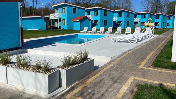 A pool area with lounge chairs and a building with blue siding. - Comfortable Holiday Home , Summer Pool (Rewal)