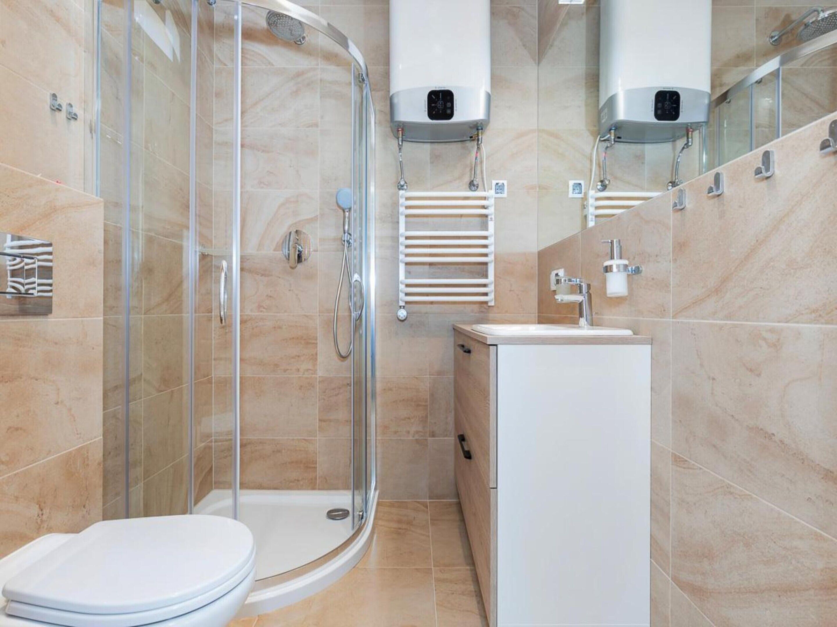 A modern bathroom with a glass-enclosed shower, a white toilet, and a sink with a mirror above it.