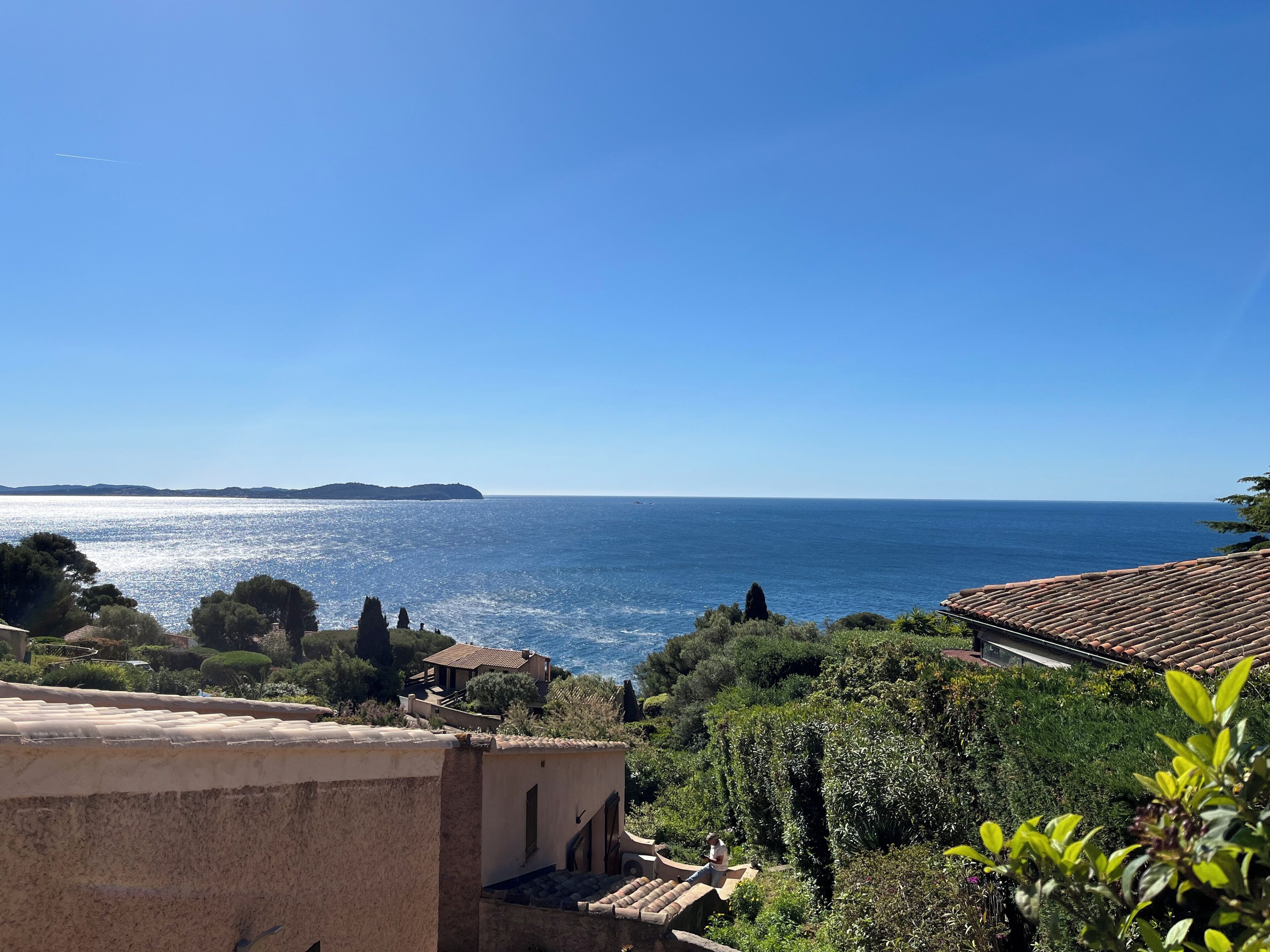 A coastal view with a clear sky, a distant island, and a building with a tiled roof.