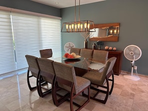 A dining area with a glass table, cushioned chairs, a pendant light, a fan, and a decorative mirror. - Private and very comfortable apartment, ideal for couples or families. (Ixtapa Zihuatanejo)