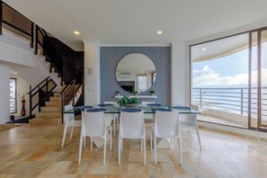 A modern dining area with a glass table, white chairs, a large mirror, and a view of the sea. - Oceanfront Triplex Penthouse: 4 Bedrooms (Cartagena de Indias)
