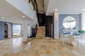 Un intérieur spacieux avec un escalier menant à un niveau supérieur, un coin repas avec une table en verre et une vue sur un bâtiment à l’extérieur.