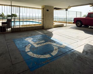 A parking area with a handicap parking space, a red car, and a view of a pool and beach. - Ocean-View Triplex Penthouse: 4 Bedrooms (Cartagena de Indias)
