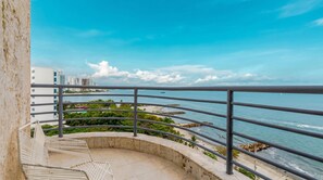 Un balcon avec vue sur la mer, une plage et des bâtiments situés au loin.