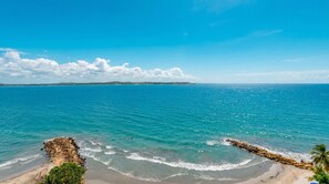 A coastal beach with clear blue waters, a rocky shoreline, and distant land. - Oceanfront Triplex Penthouse: 4 Bedrooms (Cartagena de Indias)