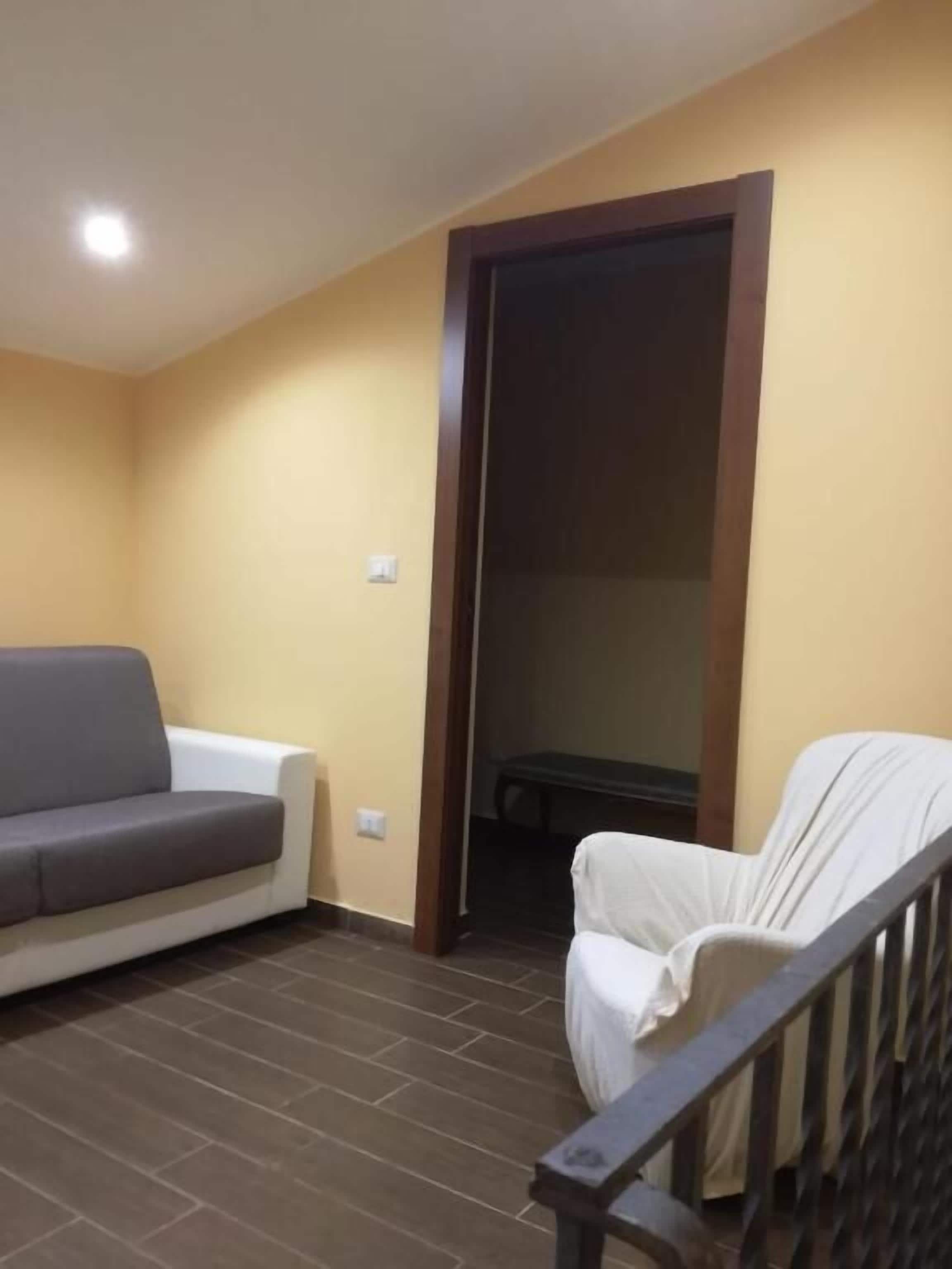 A room with a sofa, a chair, a wooden door, and a staircase.