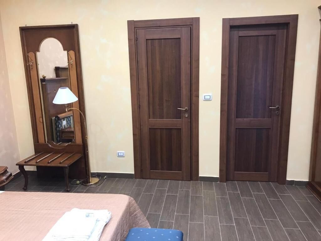 A room with a bed, a bench, a mirror, and two doors.