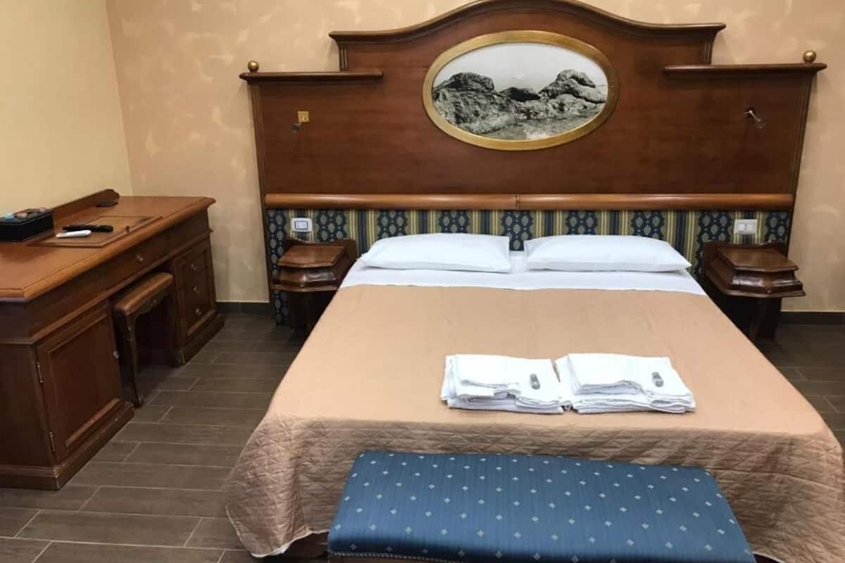 Una habitación de hotel con una cama, mesitas de noche, un escritorio y un banco.