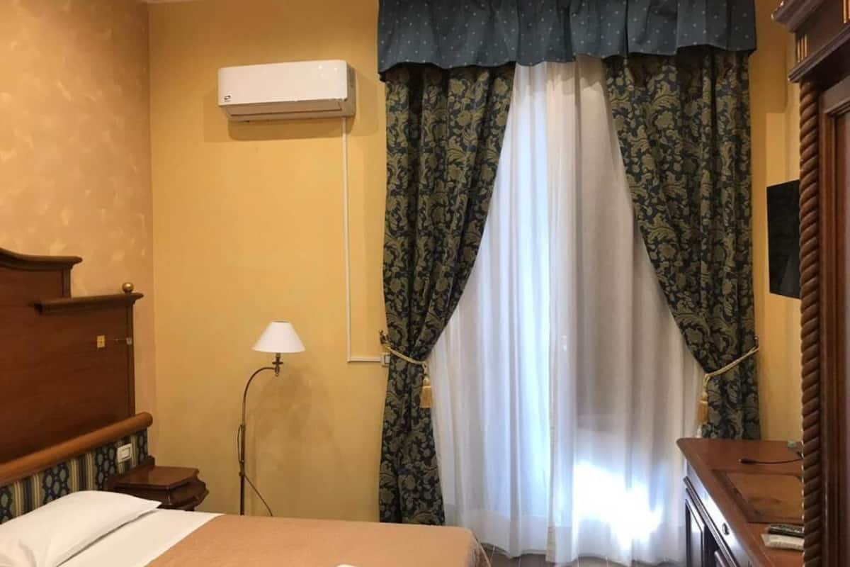 Una habitación de hotel con una cama, aire acondicionado, una lámpara y cortinas.