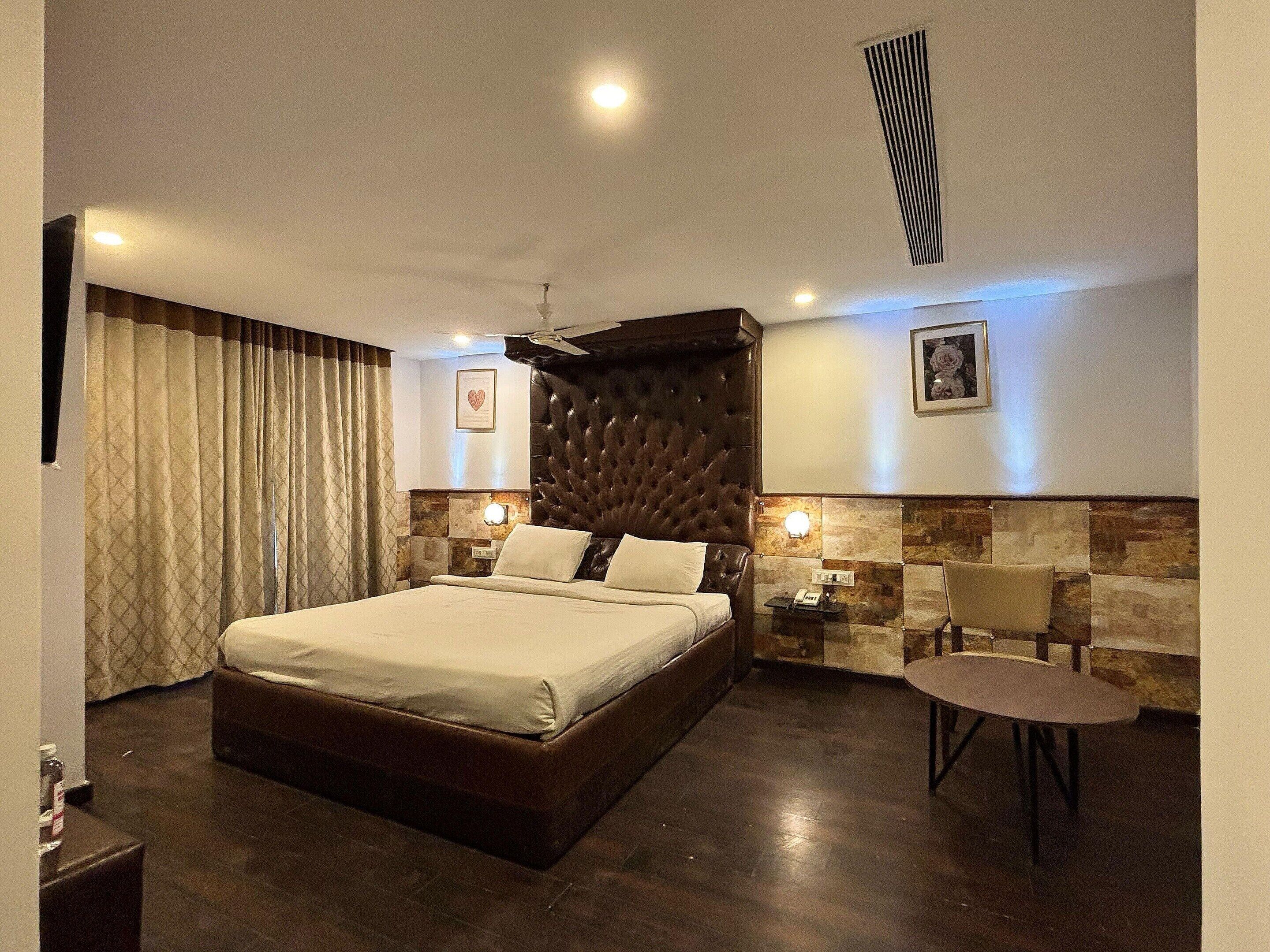 A hotel room with a large bed, a small table, a chair, a nightstand, and a wall-mounted light.
